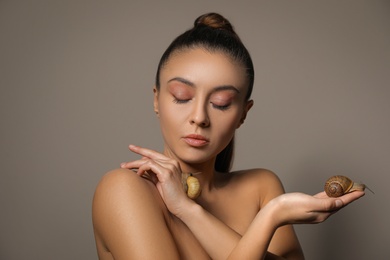 Photo of Beautiful young woman with snails on her hands against beige background