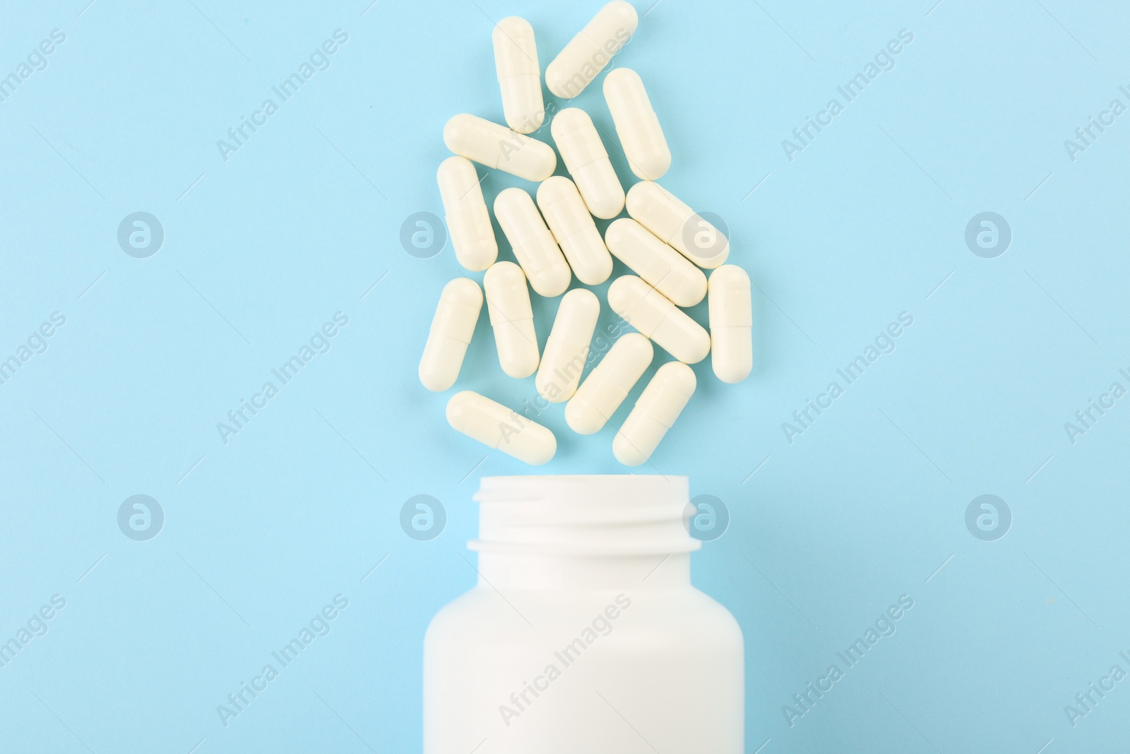 Photo of Bottle and vitamin capsules on light blue background, top view