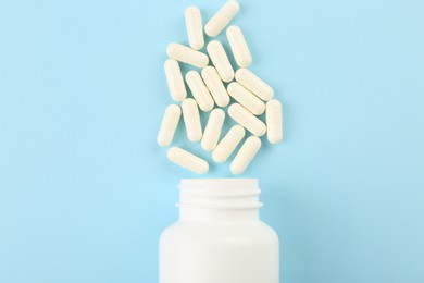 Photo of Bottle and vitamin capsules on light blue background, top view