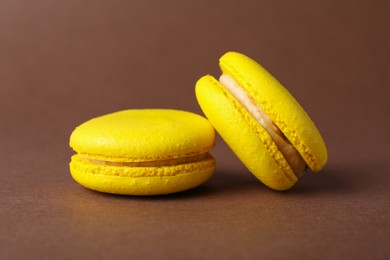 Photo of Delicious yellow macarons on brown background, closeup