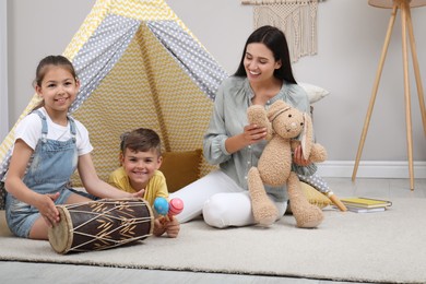 Photo of Mother and children playing near toy wigwam at home