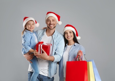 Photo of Happy family with paper bags and gift on grey background. Christmas shopping