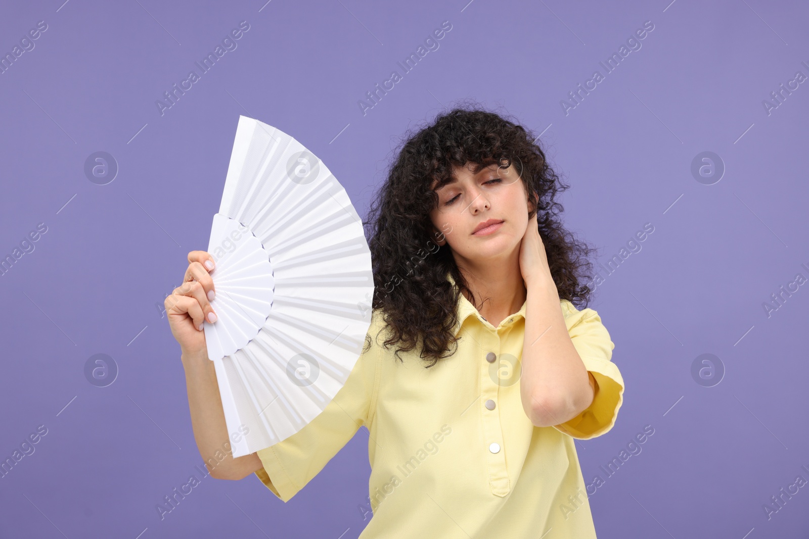 Photo of Woman with hand fan suffering from heat on purple background