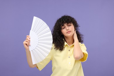 Photo of Woman with hand fan suffering from heat on purple background