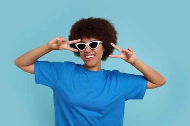 Happy young woman in stylish sunglasses on light blue background