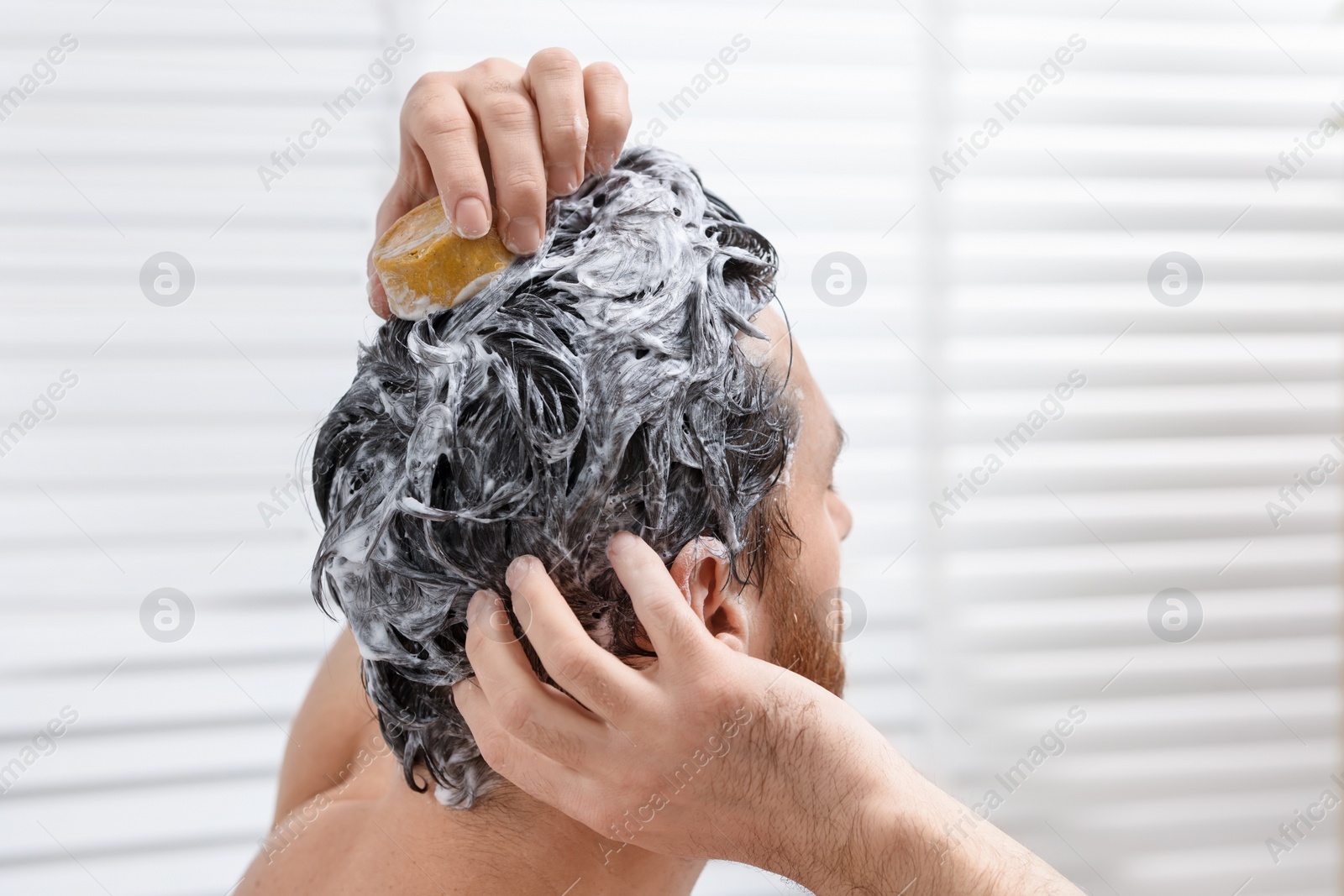 Photo of Man washing his hair with solid shampoo bar in bathroom, closeup