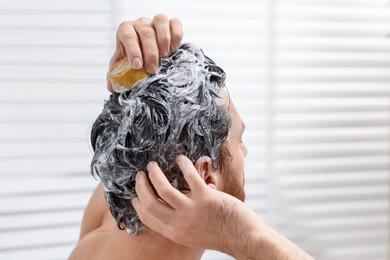 Man washing his hair with solid shampoo bar in bathroom, closeup