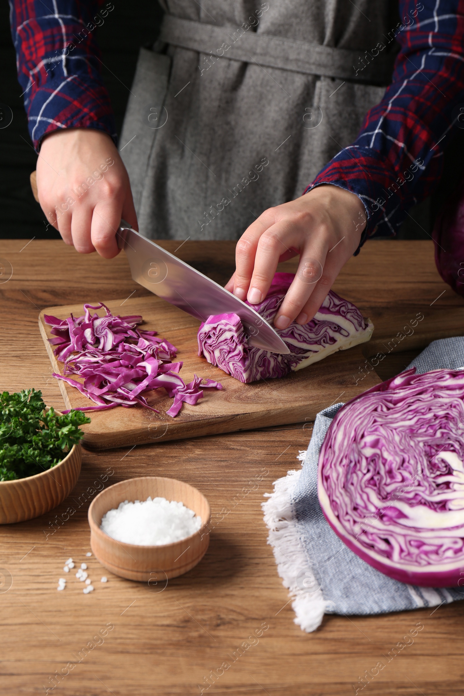 Photo of Woman cutting fresh red cabbage at wooden table, closeup