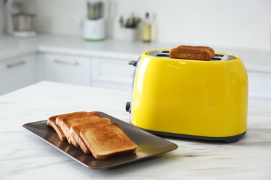 Photo of Modern toaster with slices of bread on white marble table in kitchen