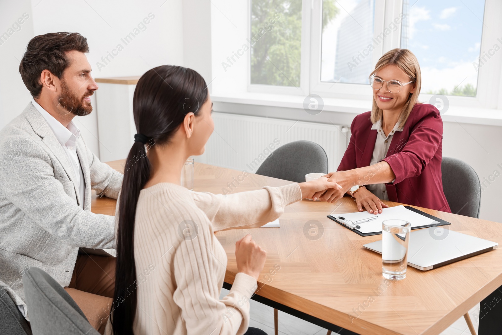 Photo of Real estate agent shaking hands with client at table in new apartment