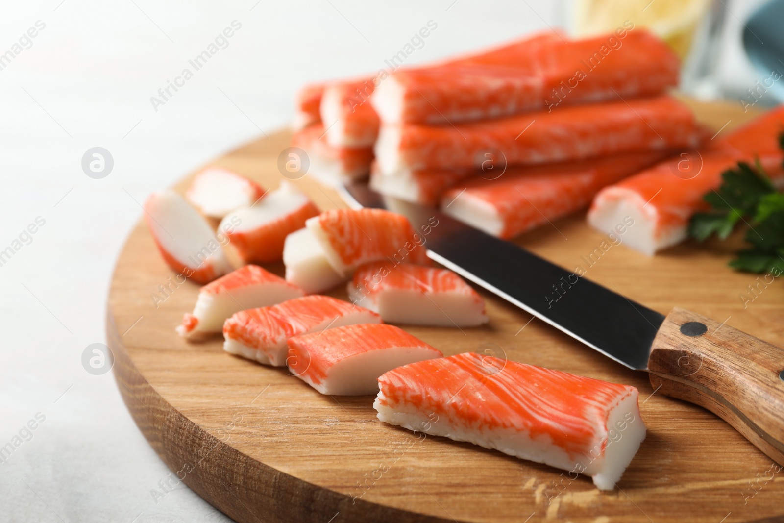Photo of Sliced crab sticks and knife on wooden cutting board, closeup