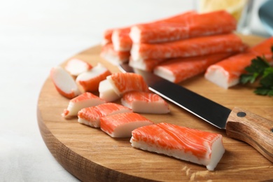 Sliced crab sticks and knife on wooden cutting board, closeup