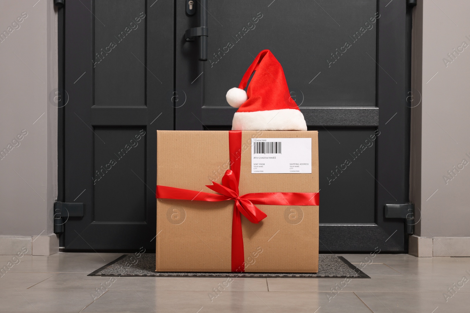 Photo of Christmas gift box and Santa hat near door indoors. Sending present by mail