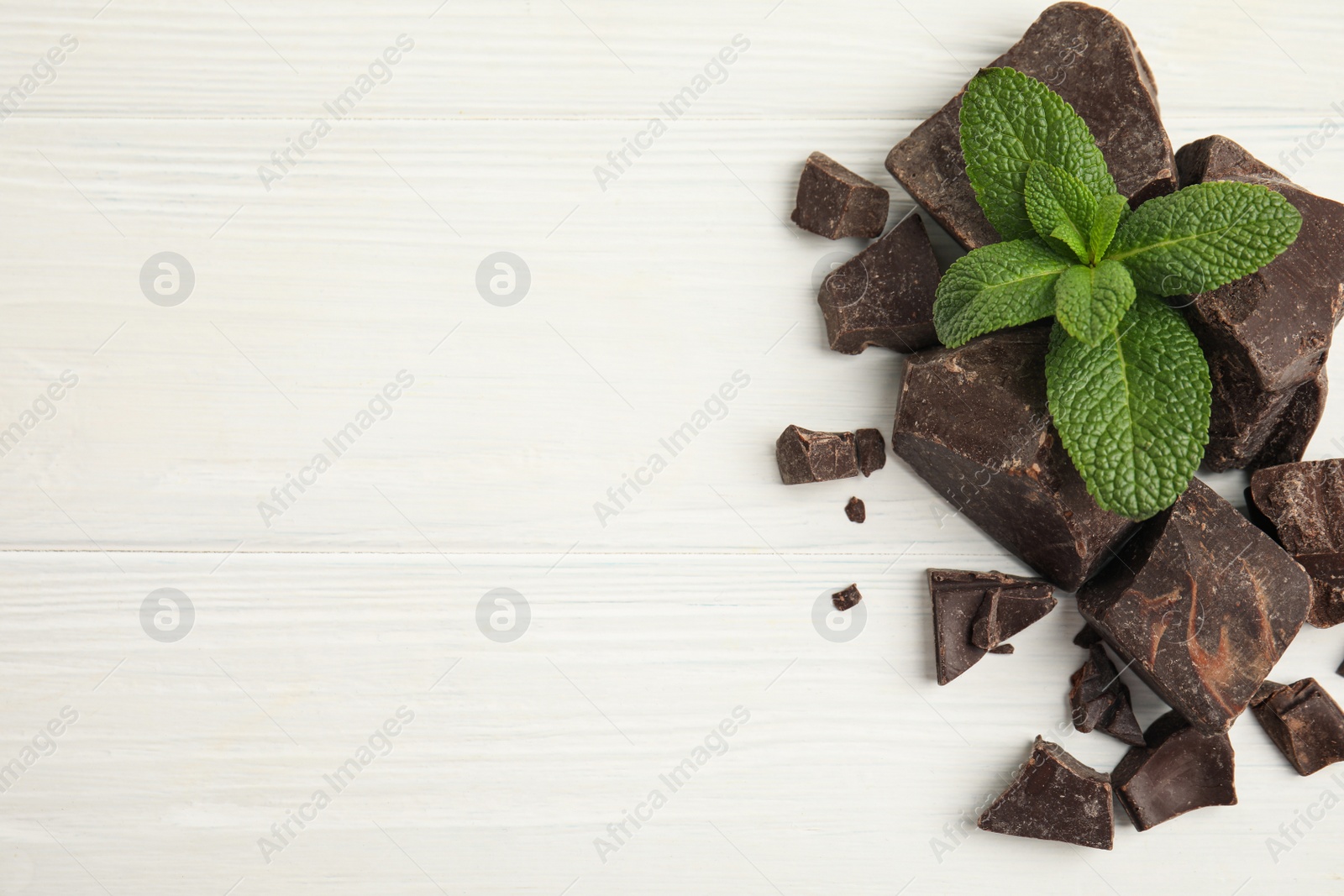 Photo of Tasty dark chocolate pieces with mint on white wooden table, flat lay. Space for text