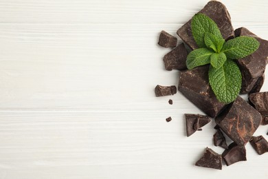 Photo of Tasty dark chocolate pieces with mint on white wooden table, flat lay. Space for text