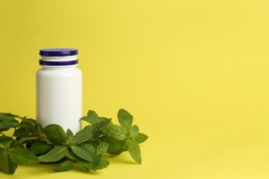 Photo of Medicine bottle near green leaves on yellow background, space for text