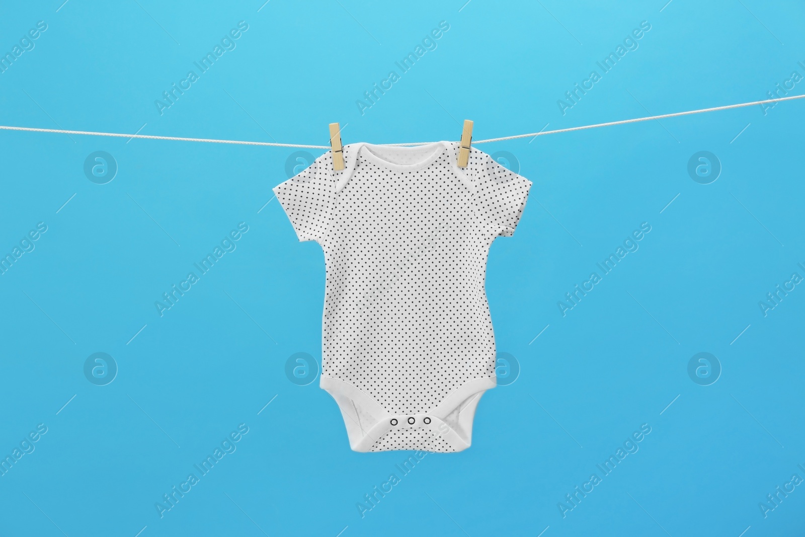 Photo of Baby onesie hanging on clothes line against blue background. Laundry day