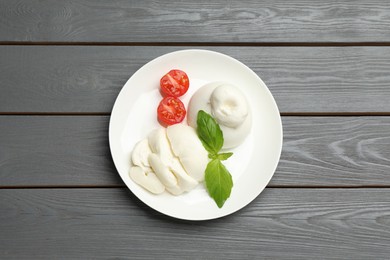 Photo of Delicious burrata cheese with basil and cut tomato on grey wooden table, top view