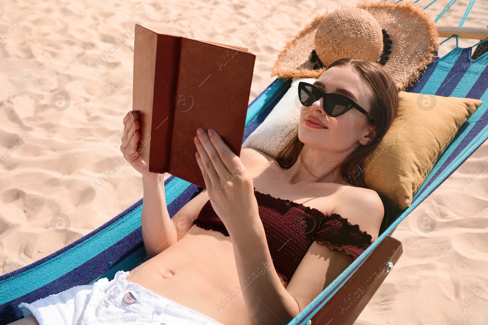 Photo of Young woman reading book in hammock on beach