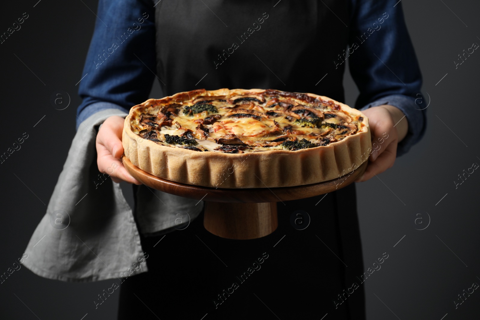 Photo of Woman holding delicious quiche with mushrooms on dark grey background, closeup