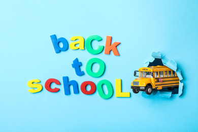 Photo of Yellow school bus and phrase "Back to school" on light blue background, flat lay. Transport for students