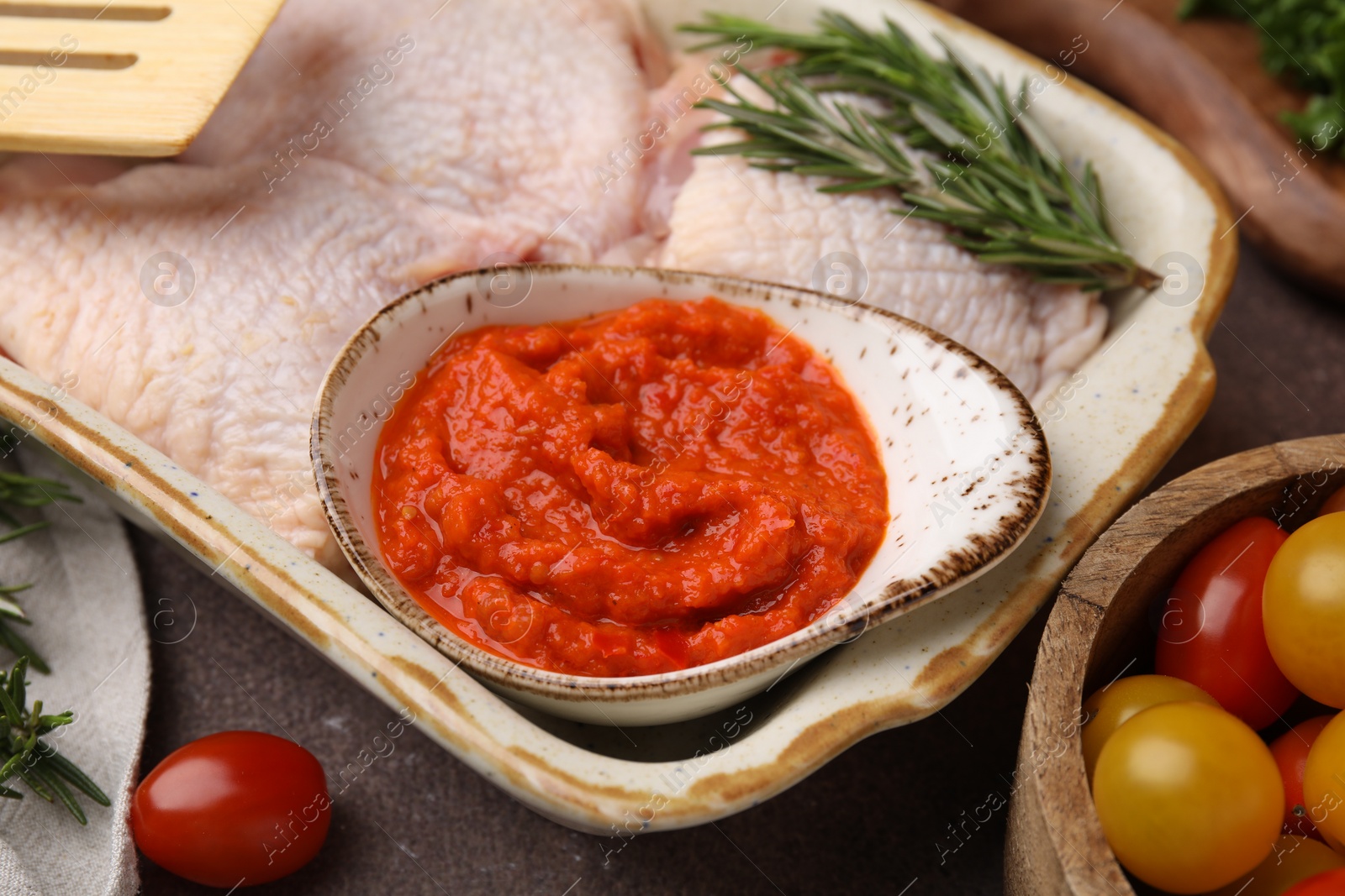 Photo of Fresh marinade, raw chicken and tomatoes on brown table, closeup