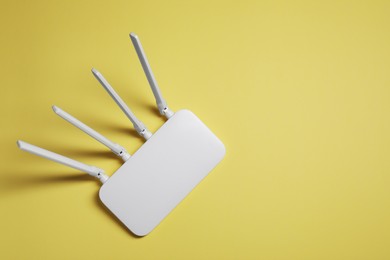 Photo of New white Wi-Fi router on yellow background, top view. Space for text