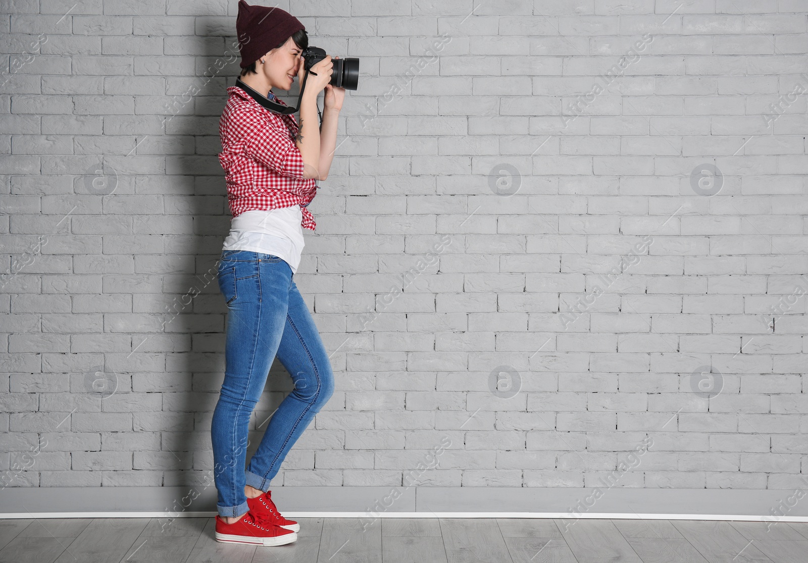 Photo of Young female photographer with camera near brick wall