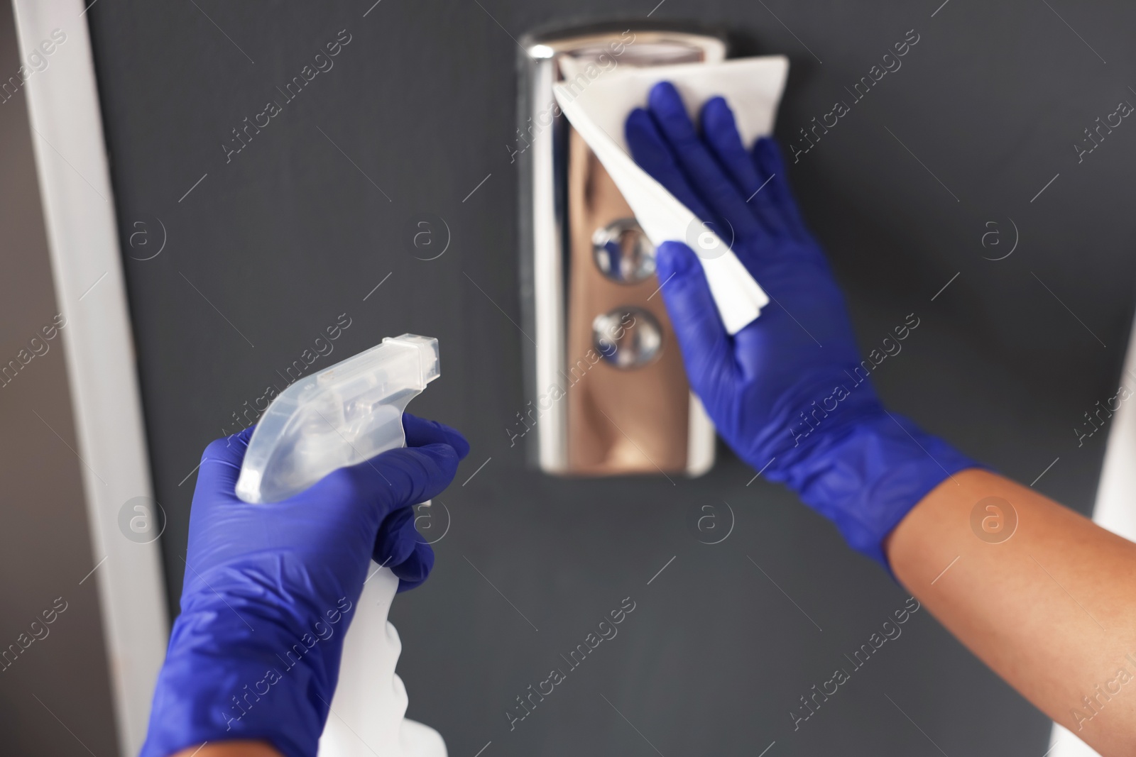 Photo of Woman wiping elevator call panel with detergent and paper napkin, closeup