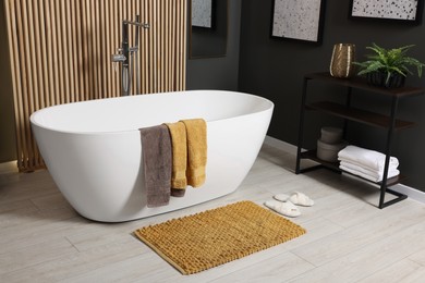 Photo of Stylish bathroom interior with bath tub, houseplant and soft yellow mat