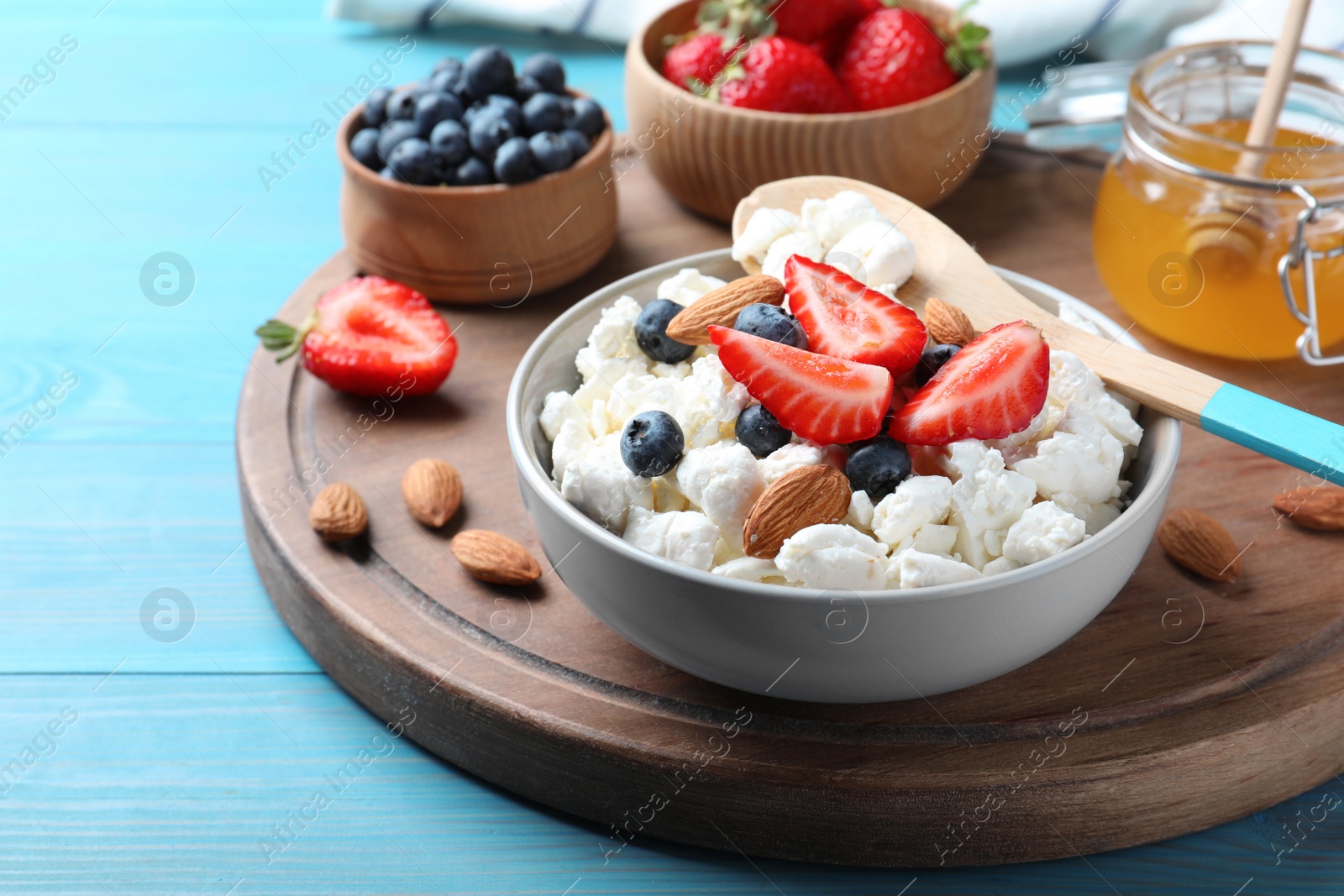 Photo of Bowl of fresh cottage cheese, berries with almond and ingredients on turquoise wooden table