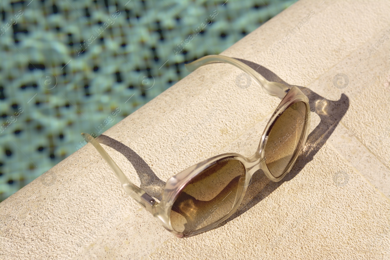 Photo of Stylish sunglasses near outdoor swimming pool on sunny day