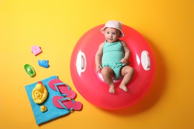 Cute little baby with inflatable ring and beach accessories on yellow background, top view