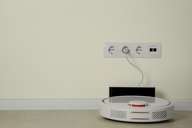 Photo of Robotic vacuum cleaner charging from electric socket on floor indoors. Space for text