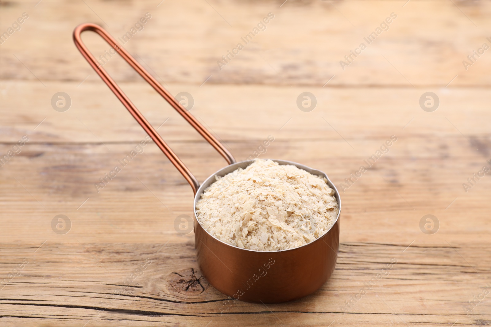 Photo of Metal small saucepan with brewer`s yeast flakes on wooden table