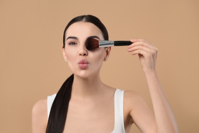 Beautiful woman with makeup brush on light brown background