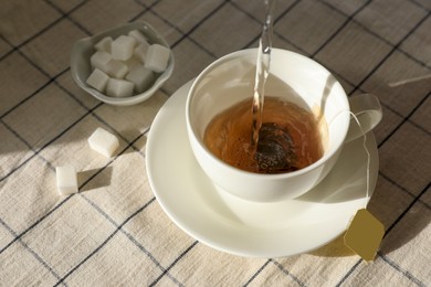 Photo of Pouring hot water into cup with tea bag on table, above view