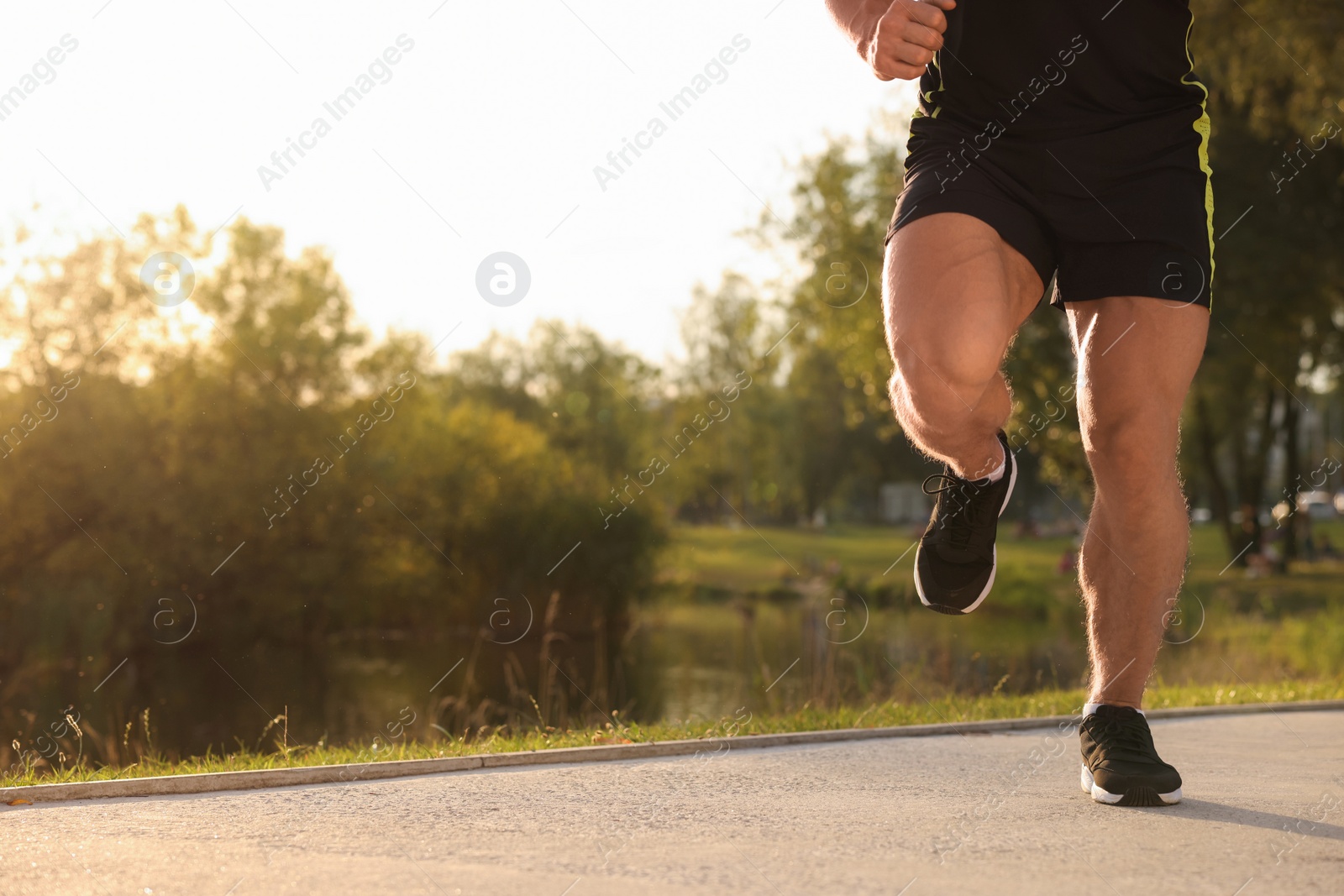 Photo of Man running near pond in park on sunny day, closeup. Space for text
