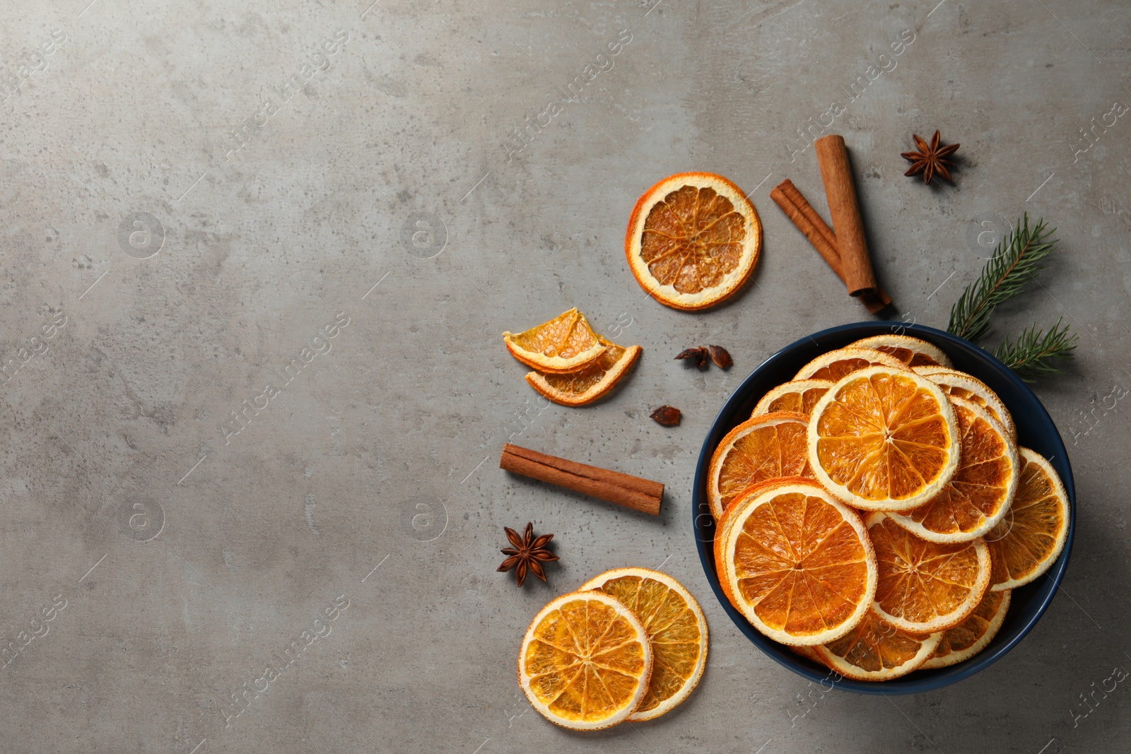 Photo of Dry orange slices, cinnamon sticks and anise stars on grey table, flat lay. Space for text