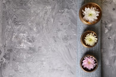 Photo of Tibetan singing bowls with water, beautiful chrysanthemum flowers on grey textured table, top view. Space for text