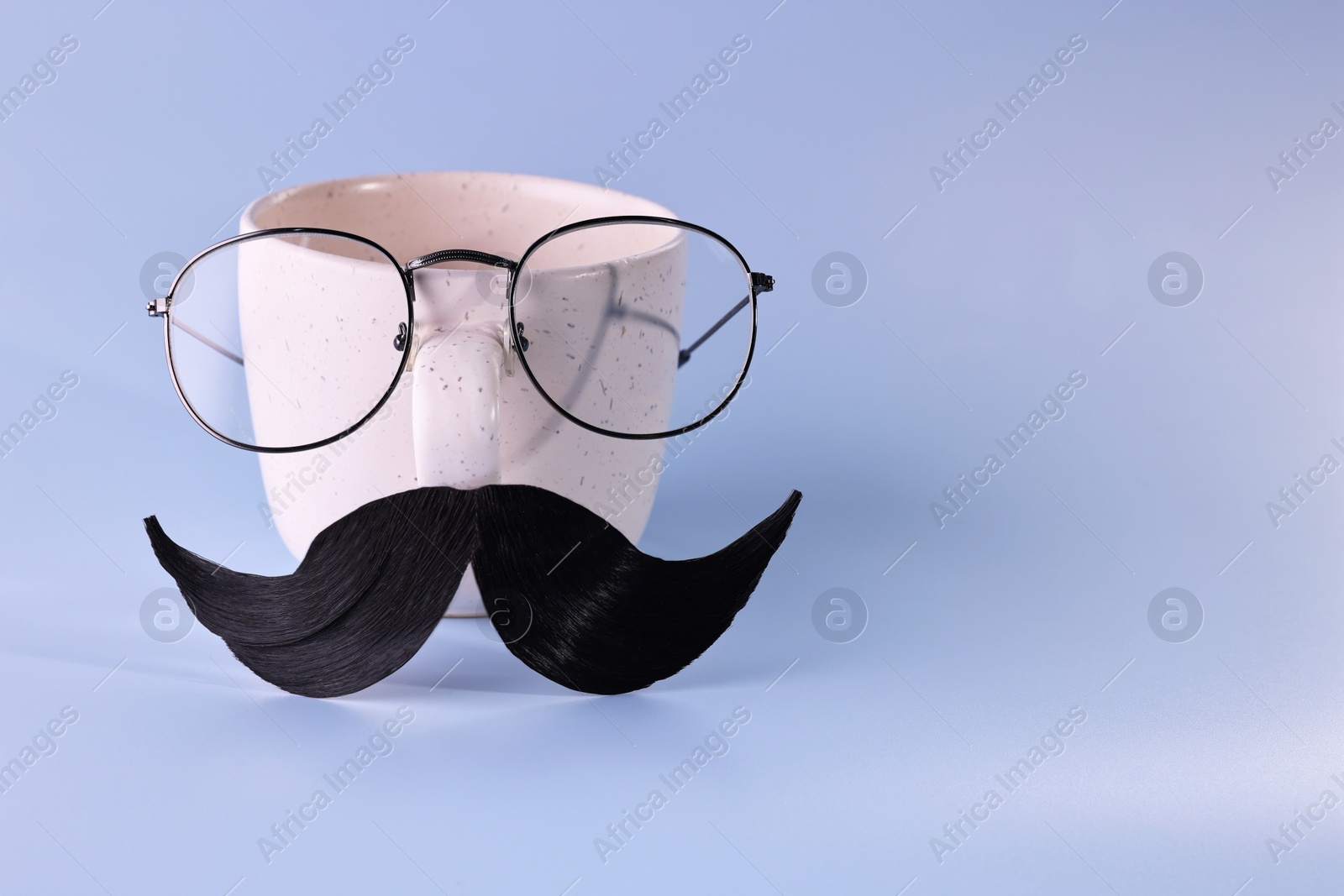 Photo of Man's face made of artificial mustache, glasses and cup on light blue background. Space for text