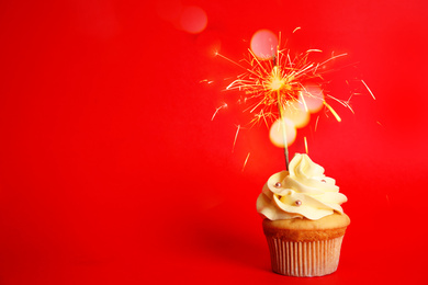 Birthday cupcake with sparkler on red background. Space for text