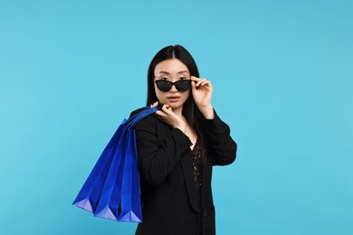 Beautiful woman with shopping bags on light blue background