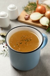 Photo of Hot delicious bouillon with dill in cup on light grey table