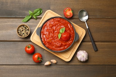 Photo of Homemade tomato sauce in bowl, spoon and ingredients on wooden table, flat lay