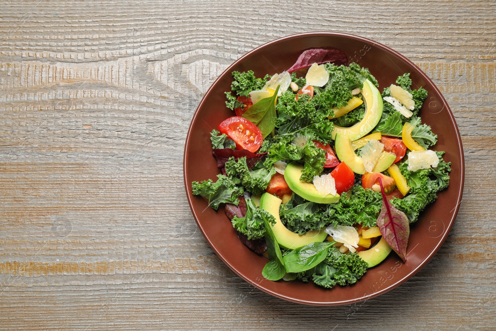 Photo of Tasty fresh kale salad on wooden table, top view. Space for text