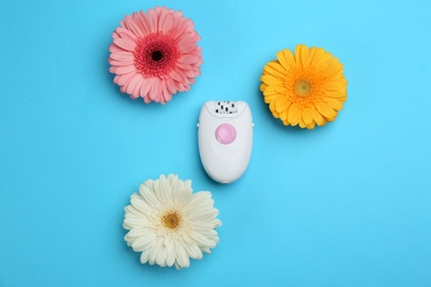 Modern epilator and flowers on blue background, flat lay