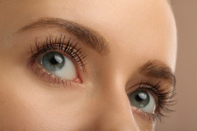 Woman with long eyelashes after mascara applying against light brown background, closeup