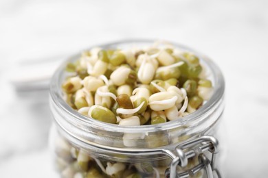 Photo of Glass jar with sprouted green mung beans on light background, closeup