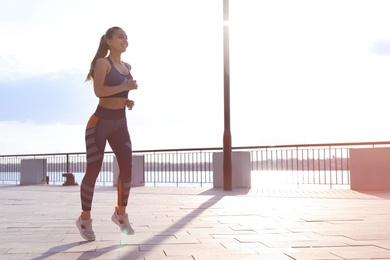 Young woman running on pier near river in morning. Space for text